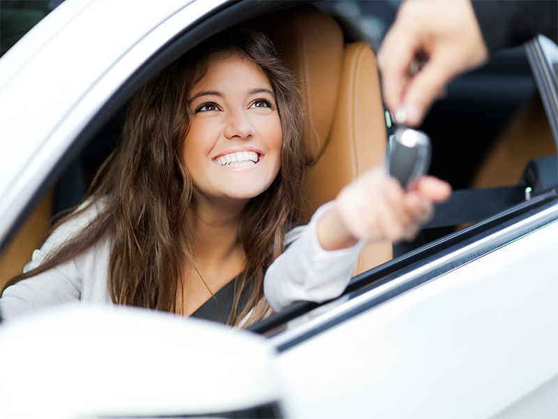 Young woman sitting in the driver's seat of a new car and holding out her hand for the key fob